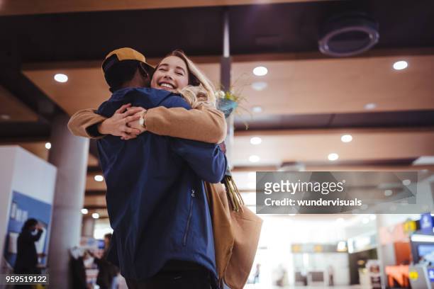 fidanzato accogliente e che abbraccia la ragazza eccitata all'aeroporto - abbracciare una persona foto e immagini stock