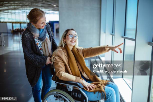 junge behinderte frau im rollstuhl und mutter warten am flughafen - adult helping teenager stock-fotos und bilder