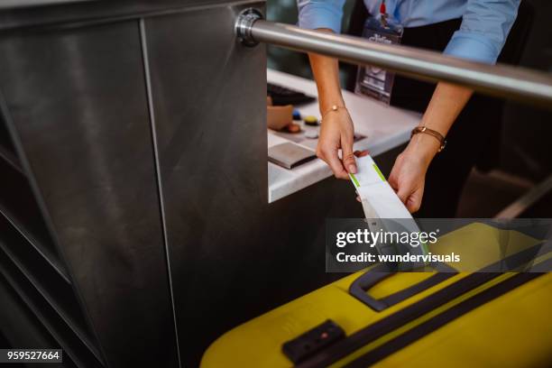 airport check-in counter employee attaching tag on luggage - bagagem imagens e fotografias de stock