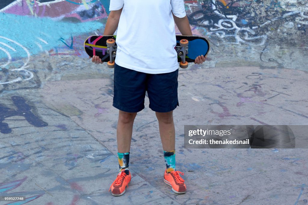 Crop of woman holding skateboard behind back