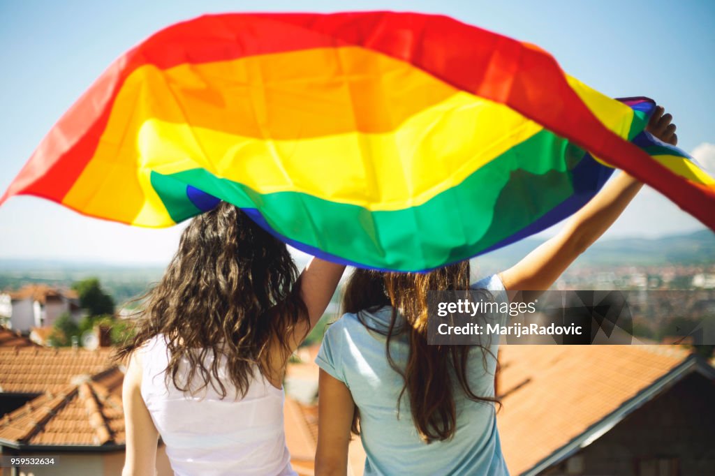 Concepto de felicidad de LGBT lesbianas pareja momentos. Sosteniendo la bandera del arco iris al aire libre