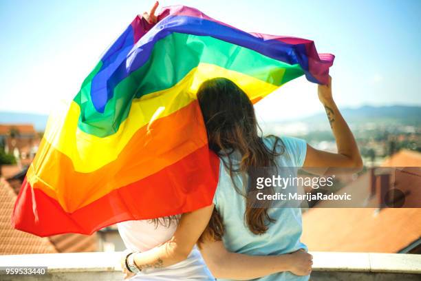 lgbt-lesbisches paar momente glück konzept. regenbogenfahne halten im freien - marijaradovic stock-fotos und bilder