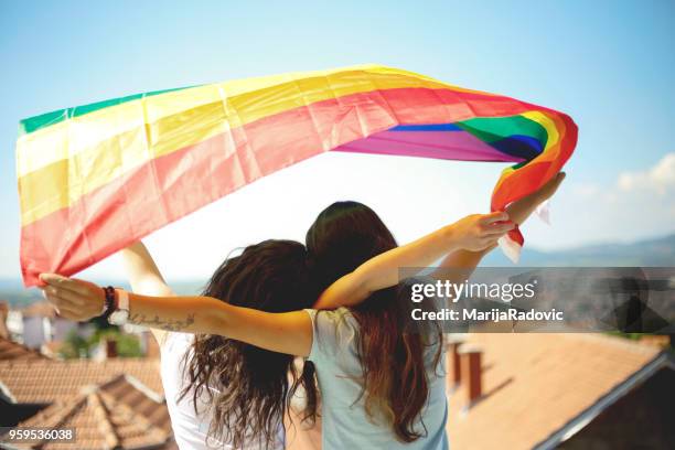 lgbt-lesbisches paar momente glück konzept. regenbogenfahne halten im freien - marijaradovic stock-fotos und bilder