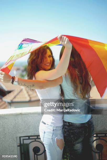 lgbt-lesbisches paar momente glück konzept. regenbogenfahne halten im freien - marijaradovic stock-fotos und bilder