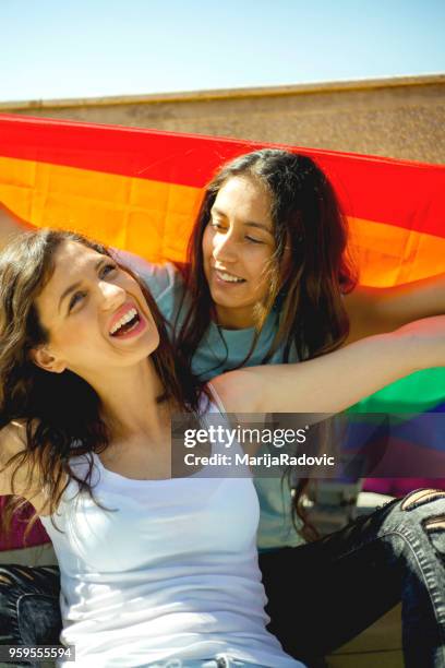 lgbt-lesbisches paar momente glück konzept. regenbogenfahne halten im freien - marijaradovic stock-fotos und bilder