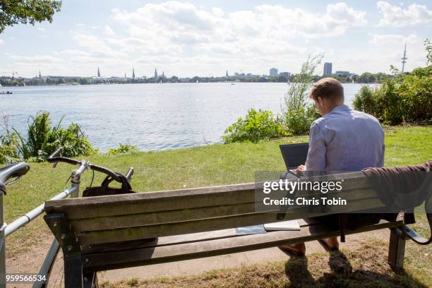 young business man working on laptop on bench in city park with lake - alster river stock pictures, royalty-free photos & images