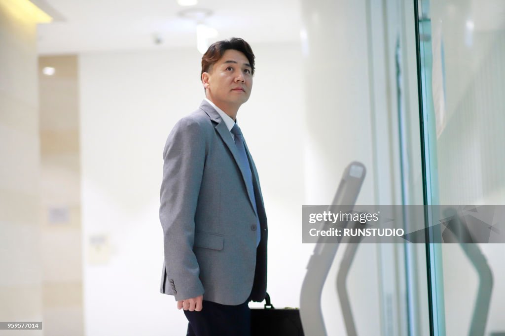 Middle aged businessman waiting for elevator in office corridor