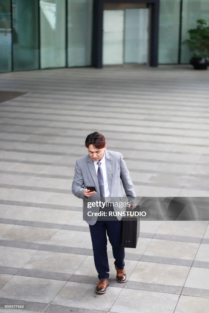 Middle aged businessman using smartphone  outside office building