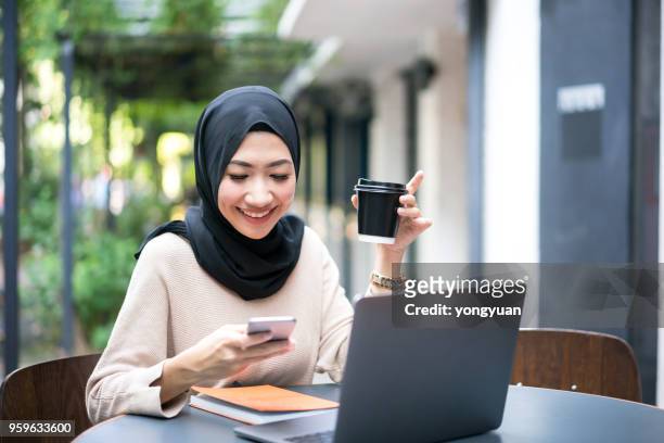 lächelnde malaysische mädchen mit ihrem smartphone - student girl using laptop computer and smart phone stock-fotos und bilder