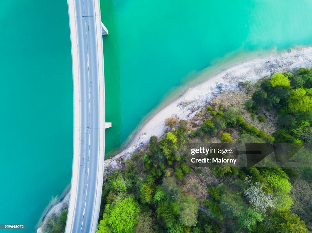 Aerial view on turquoise Lake Sylvenstein and forest with road on the bay leading over the water. Germany, Bavaria, Lake Sylvenstein