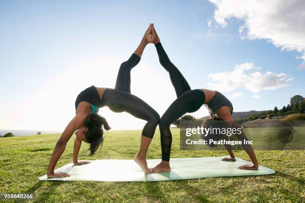 two women doing acro yoga in green field - acroyoga stock pictures, royalty-free photos & images