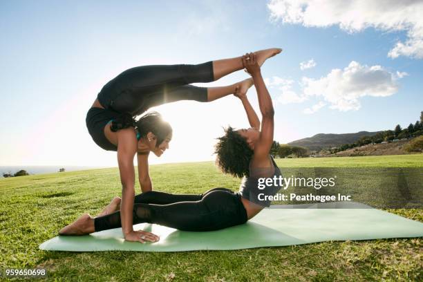 two women doing acro yoga in green field - acroyoga stock pictures, royalty-free photos & images