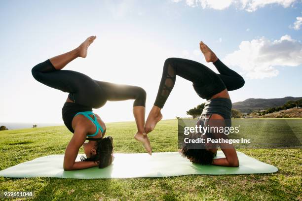 two women doing acro yoga in green field - acroyoga stock pictures, royalty-free photos & images