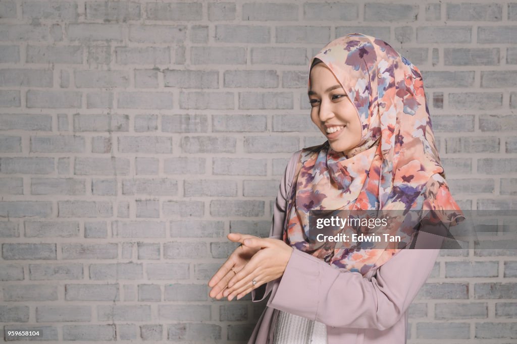 A malay female wearing traditional clothes and tudung doing a greeting hand gesture for Ramadan season