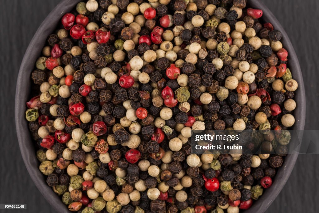 Bowl of various pepper peppercorns seeds mix on dark stone