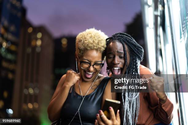 multiethniques amis célébrant les bonnes nouvelles sur mobile - femmes africaines photos et images de collection