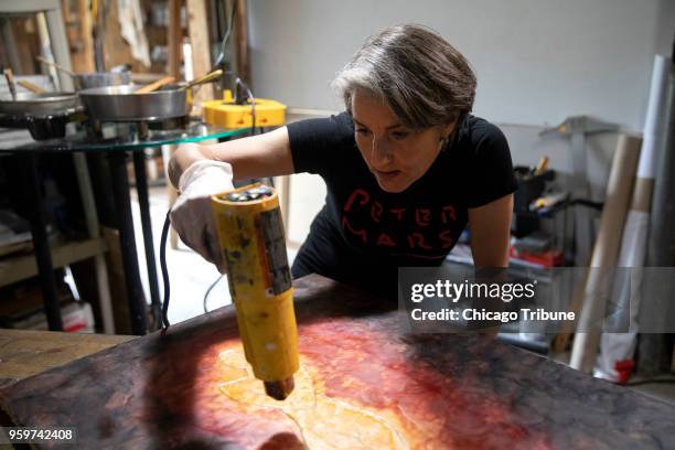 Using a heat gun, Kelly Mathews works on a piece of art with paint and beeswax in her basement studio on Monday, May 14 in Chicago, Ill. Mathews, who...