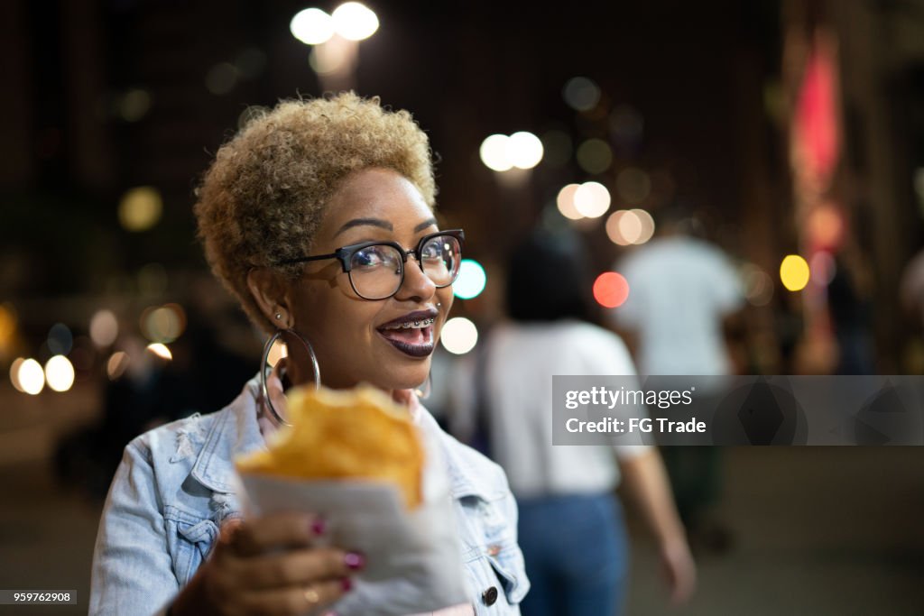 Jovem mulher comendo Pastel na rua depois do trabalho