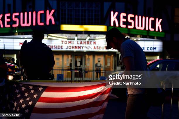 An American Flag is light by headlights of a Police cruiser as protestors and fans face off on opposing sides of the street ahead of a tour stop by...
