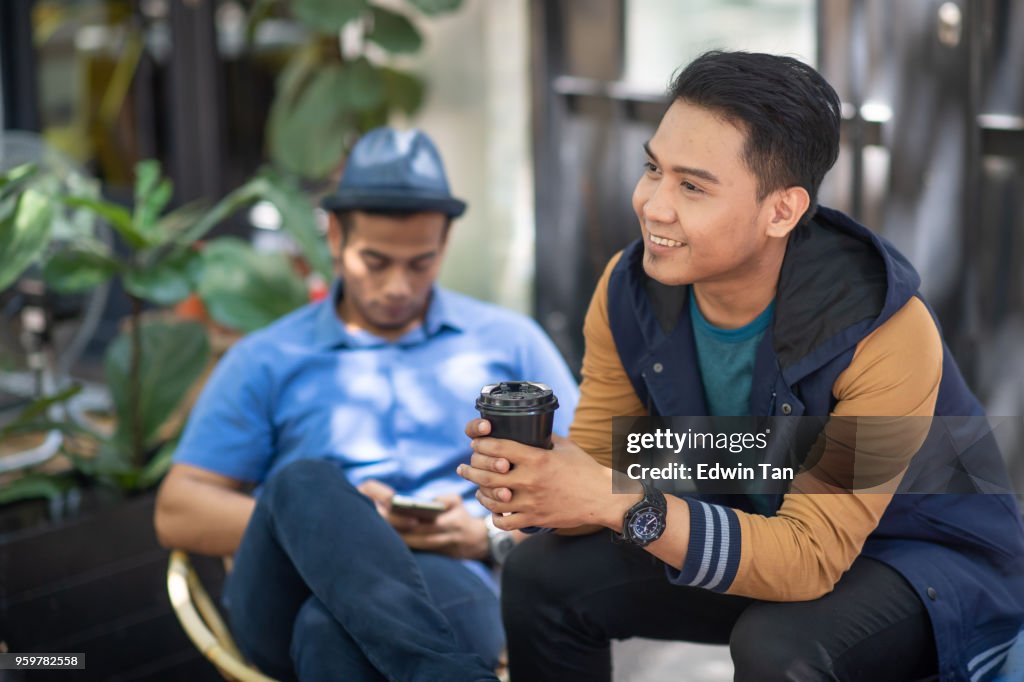 2 malay males sitting down at road side and talking to each other bonding time