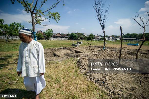 Man walks past a graveyard, where villagers filled in graves planned for individuals who were involved in the Surabaya suicide bombings, in Surabaya,...