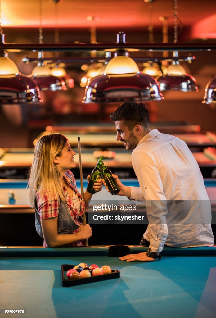 Happy couple toasting with beer while playing snooker in a bar.