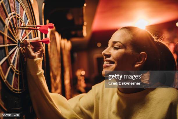 young happy woman taking darts out of dart board. - dart stock pictures, royalty-free photos & images