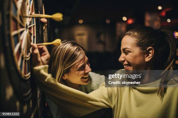 happy women talking while removing darts from dartboard. - pub darts stock pictures, royalty-free photos & images