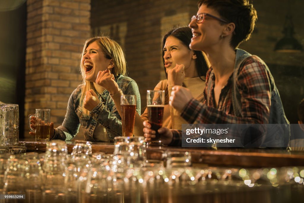 Mulheres alegres se divertindo enquanto assistia a um jogo de esportes na TV em um bar.