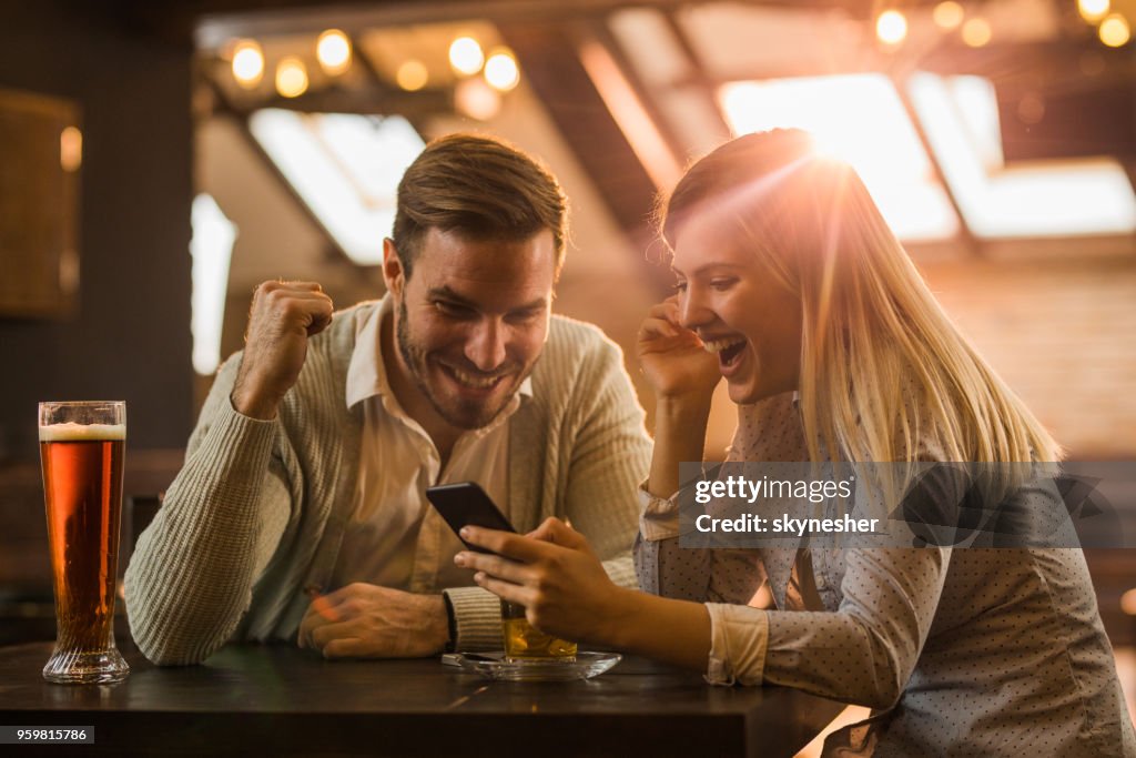 Feliz pareja sentada en un café y leyendo un sorprendente mensaje de texto en el teléfono celular.