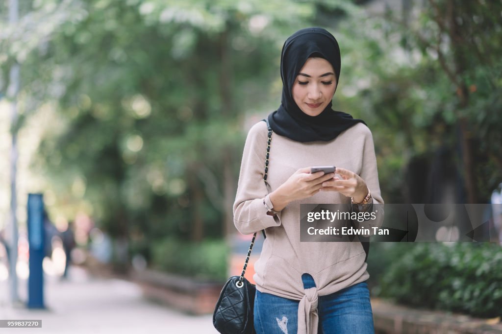 Atractiva señora malaya con pañuelo en la cabeza en el teléfono que se comunican
