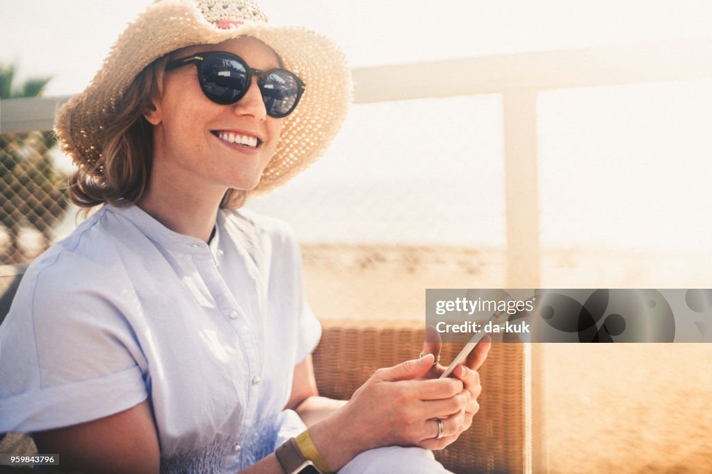 Usando el teléfono inteligente de vacaciones al atardecer por una mujer bonita