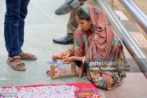 Woman strings beads on colourful string to make necklaces to sell to passersby along the roadside in Chennai, Tamil Nadu, India.