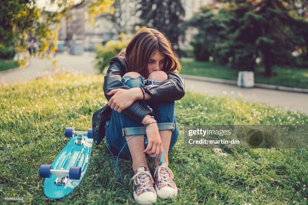 Depresión adolescente con patineta sentado en la hierba