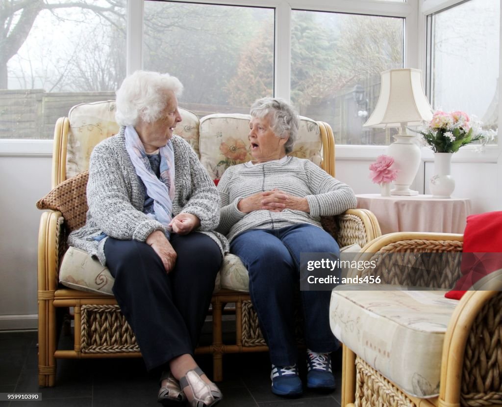 Duas mulheres sênior sentado no sol de quarto /conservatory