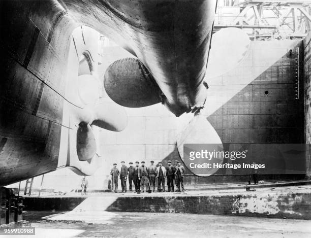 Workers pose near the port and centre propellers of the ocean liner, RMS Olympic, in the Thompson Graving Dock during fitting out at the Harland and...