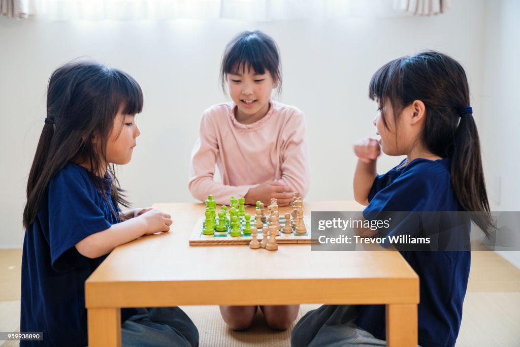 Twin girls playing chess together while older sister watches