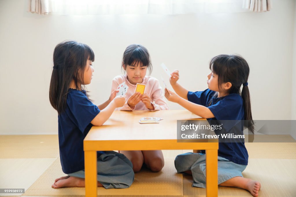Twin girls playing cards together while older sister watches