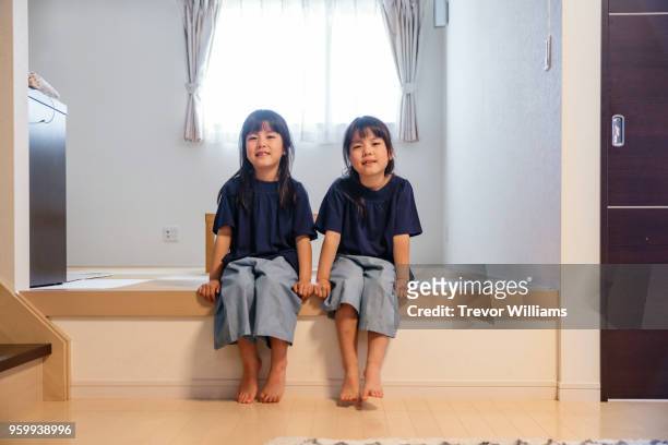 twin girls sitting together in a living room - asian twins stockfoto's en -beelden