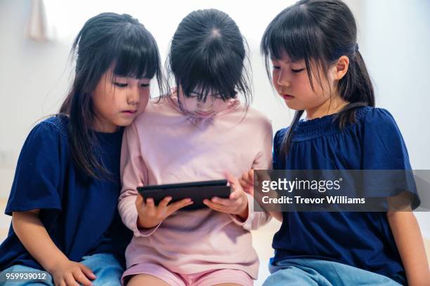 twin girls looking at a digital tablet with older sister - digital twin stock pictures, royalty-free photos & images