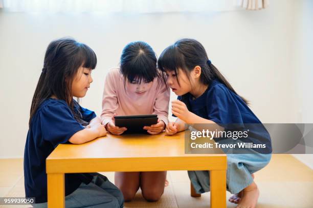 twin girls looking at a digital tablet with older sister - digital twin bildbanksfoton och bilder