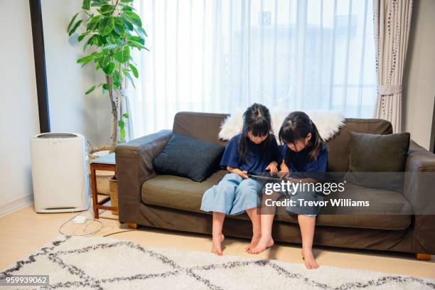 twin girls looking at a digital tablet on a sofa - digital twin stock pictures, royalty-free photos & images