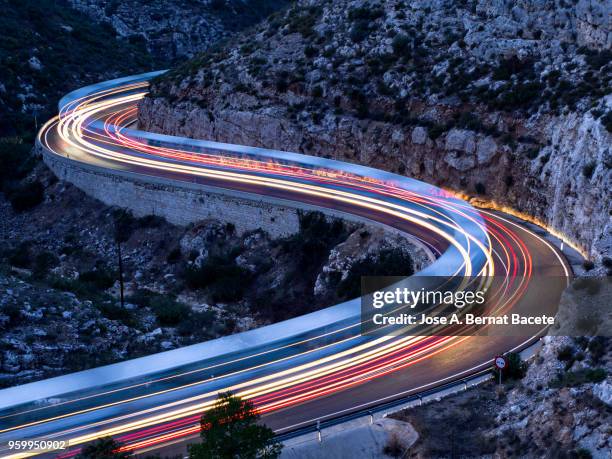 lights and trails of vehicles, cars and trucks, circulating along a road of mountain between ravines with circular curves closed in the nightfall. - tweebaansweg stockfoto's en -beelden