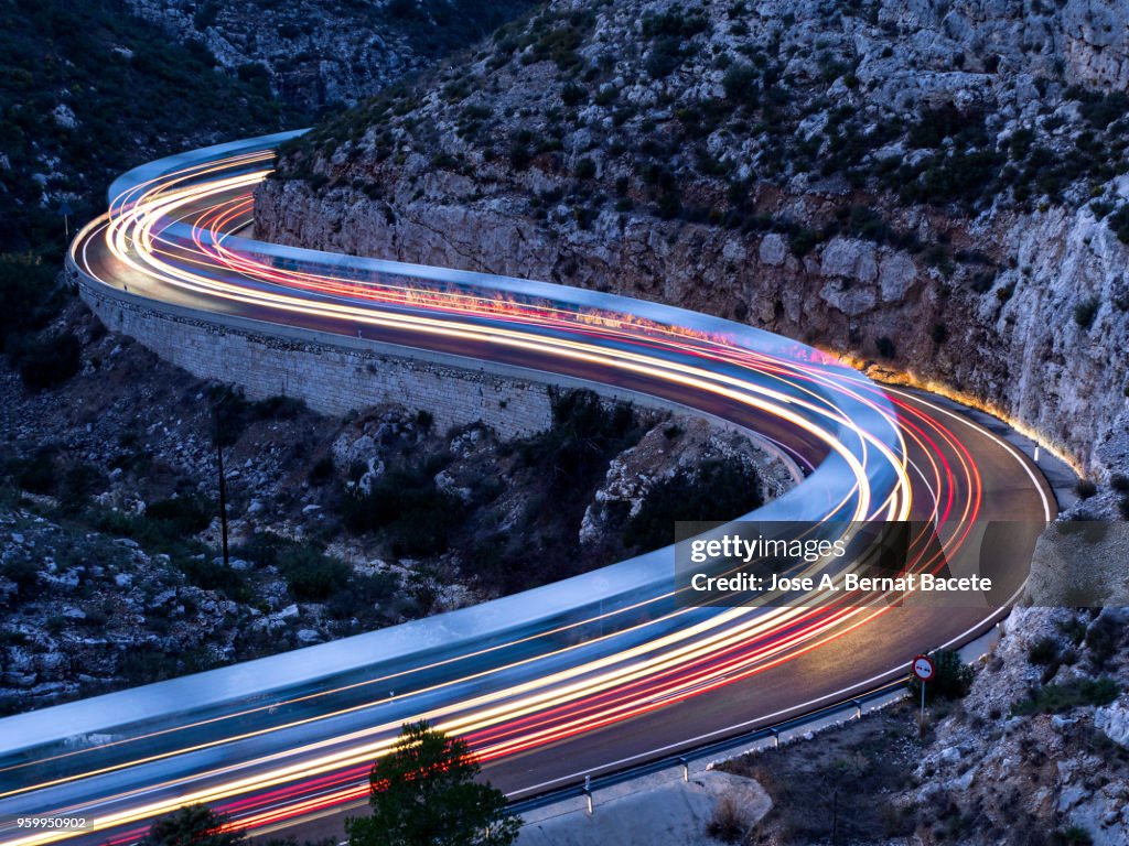 Lights and trails of vehicles, cars and trucks, circulating along a road of mountain between ravines with circular curves closed in the nightfall.