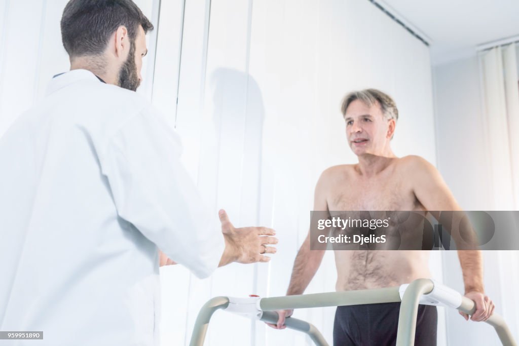 Doctor helping mature patient walk after operation.