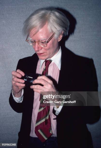 View of American Pop artist Andy Warhol as he looks at his Olympus-brand 35mm film camera at the Paradise Garage night club, New York , New York,...