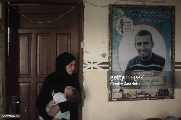 Intisar Abu Salah , Fadi's mother holds one of Fadi Abu Salah's children near his poster on the first days of holy Islamic month of Ramadan in Khan...
