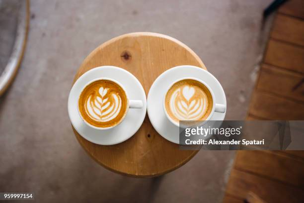 two coffee cups with latte art on a round wooden table, directly above - symmetry stock pictures, royalty-free photos & images
