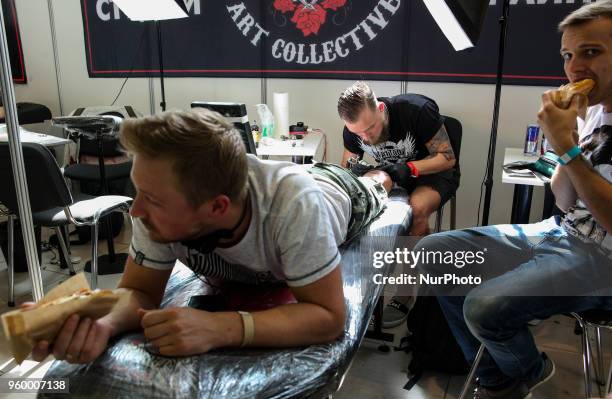 Men eat hot-dogs while tattoo artist makes a tattoo for one of them during the International Tattoo Convention &quot;Tattoo Collection 2018&quot; in...