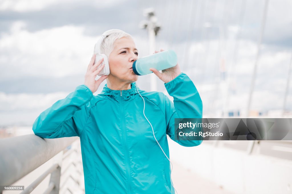 Mature female jogger with headphones drinking water